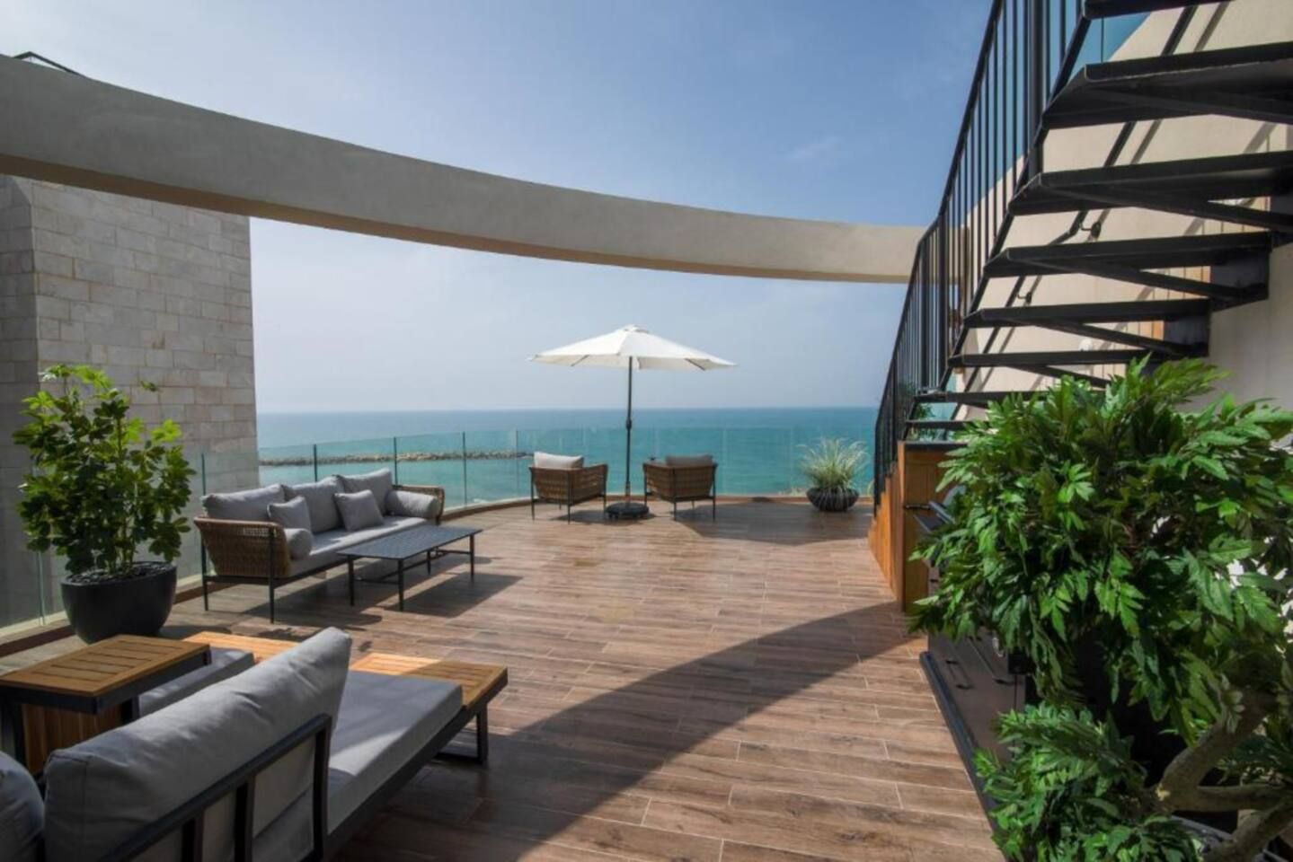 A modern outdoor seating area with a view of the sea, featuring a sofa, chairs, and a table.