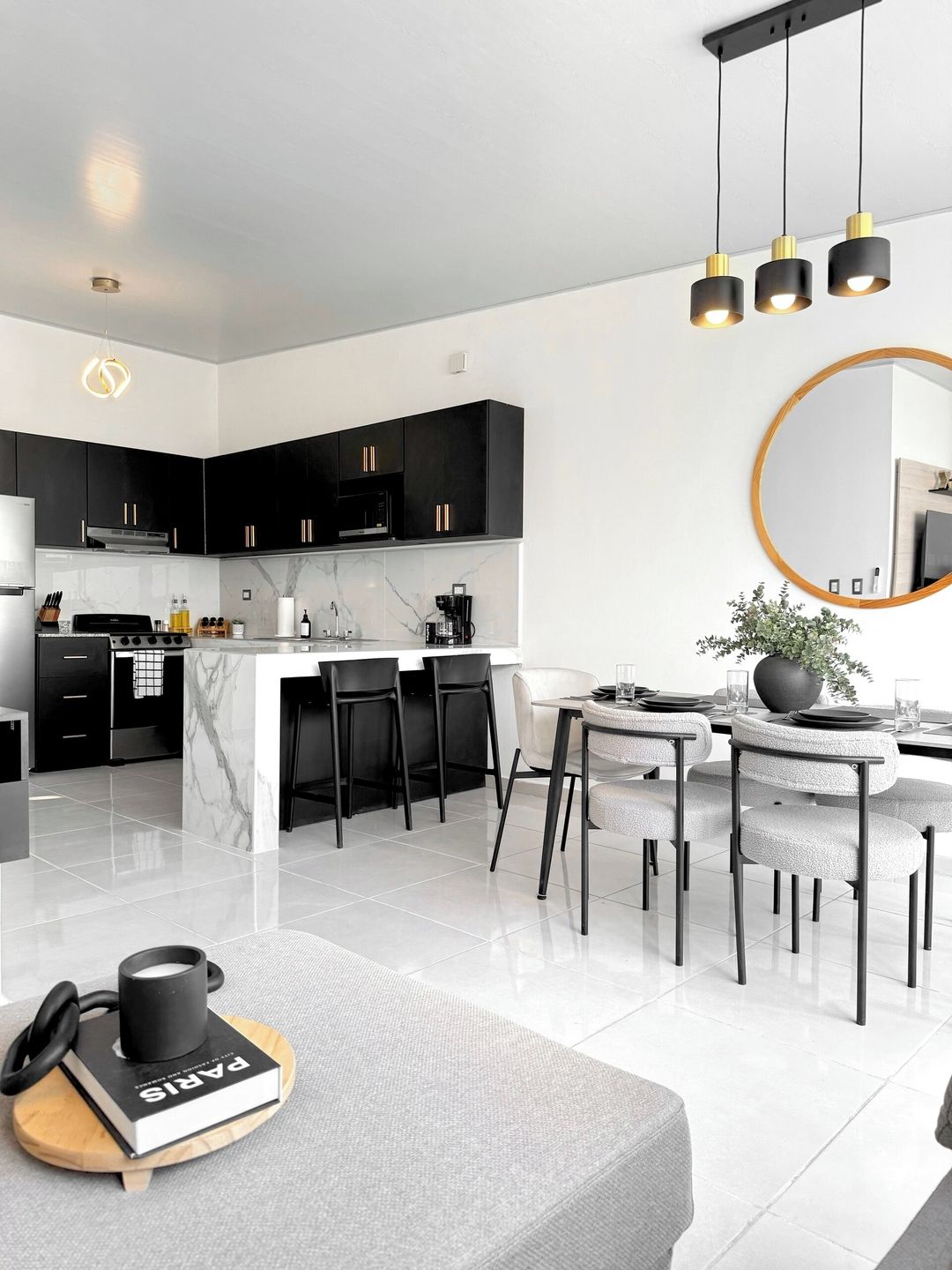 A modern kitchen with black cabinets, a marble island, and a dining area with white chairs.