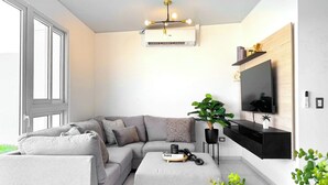 Uma sala de estar moderna com sofá seccional, mesa de centro, TV fixada numa parede de madeira e uma janela grande.