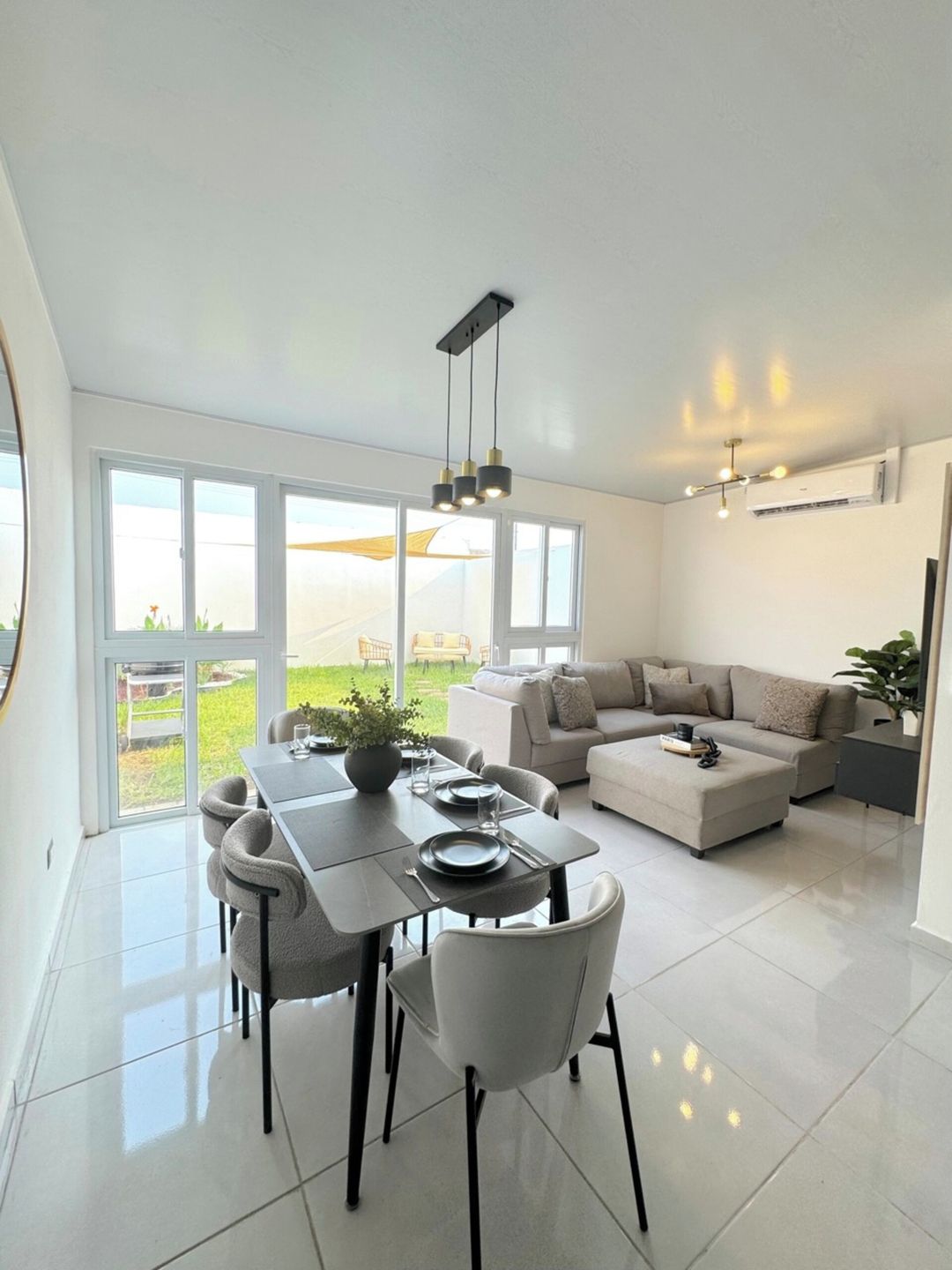 A modern living room with a dining area, large windows, and a flat-screen TV.