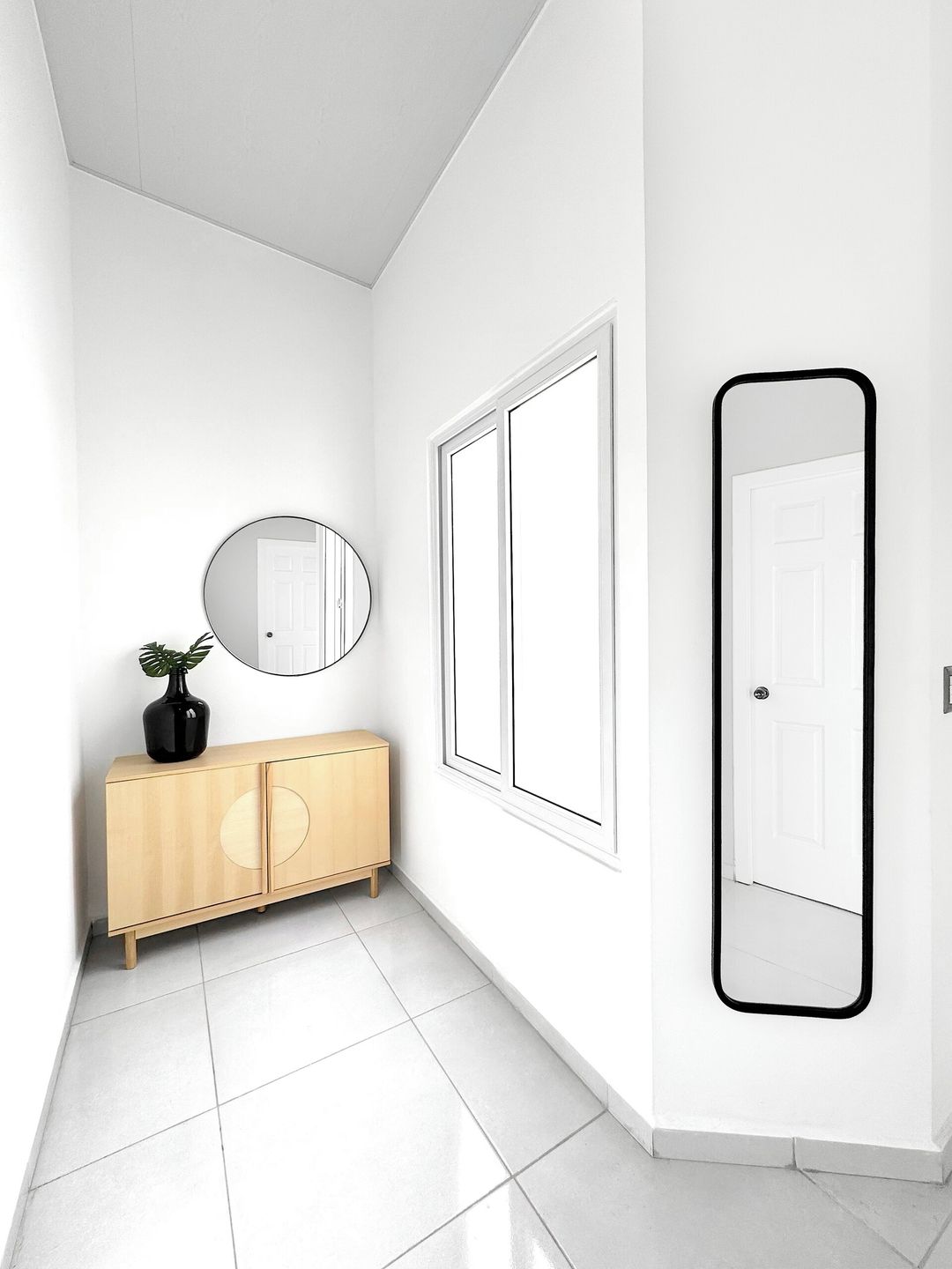 A hallway with a wooden cabinet, a round mirror, and a door.