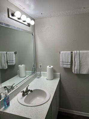 Un bagno con un lavandino bianco, uno specchio illuminato e asciugamani appesi al muro.