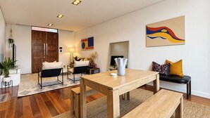 A modern living room with a wooden dining table, black chairs, a sofa with patterned cushions, and a large abstract painting on the wall. - Wake up and walk to the Sunday market (Alphington)
