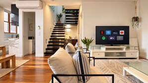 A modern living room with a sofa, a flat-screen TV, a staircase, and a kitchen area. - Wake up and walk to the Sunday market (Alphington)