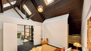 A bedroom with a large bed, a nightstand, a window with a view, and a door leading to another room. - Wake up and walk to the Sunday market (Alphington)
