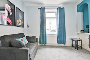A living room with a grey sofa, teal curtains, a small round table, and a framed zebra picture. - 2BR Designer Home near Swansea City Centre (Swansea)