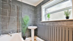 A bathroom with a bathtub, a sink, a radiator, and a window with plants. - 2BR Designer Home near Swansea City Centre (Swansea)