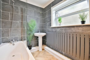 A bathroom with a bathtub, a sink, a radiator, and a window with plants. - 2BR Designer Home near Swansea City Centre (Swansea)