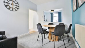 A modern room with a round table, four chairs, a wall clock, and a window with curtains. - 2BR Designer Home near Swansea City Centre (Swansea)