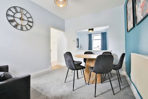 A modern room with a round table, four chairs, a wall clock, and a window with curtains. - 2BR Designer Home near Swansea City Centre (Swansea)
