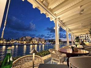 A waterfront patio with outdoor seating, a view of the sea, and buildings in the background. - Junior Suite at Fishing Lodge Cap Cana (Punta Cana)