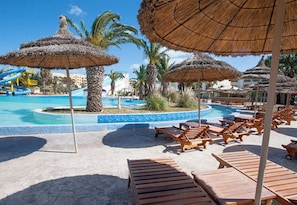 A resort pool area with lounge chairs and thatched umbrellas.