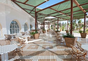 An outdoor cafe with tables and chairs, a tiled floor, and a covered area with a metal roof. - Soviva Resort & Aquapark (Port El Kantaoui)
