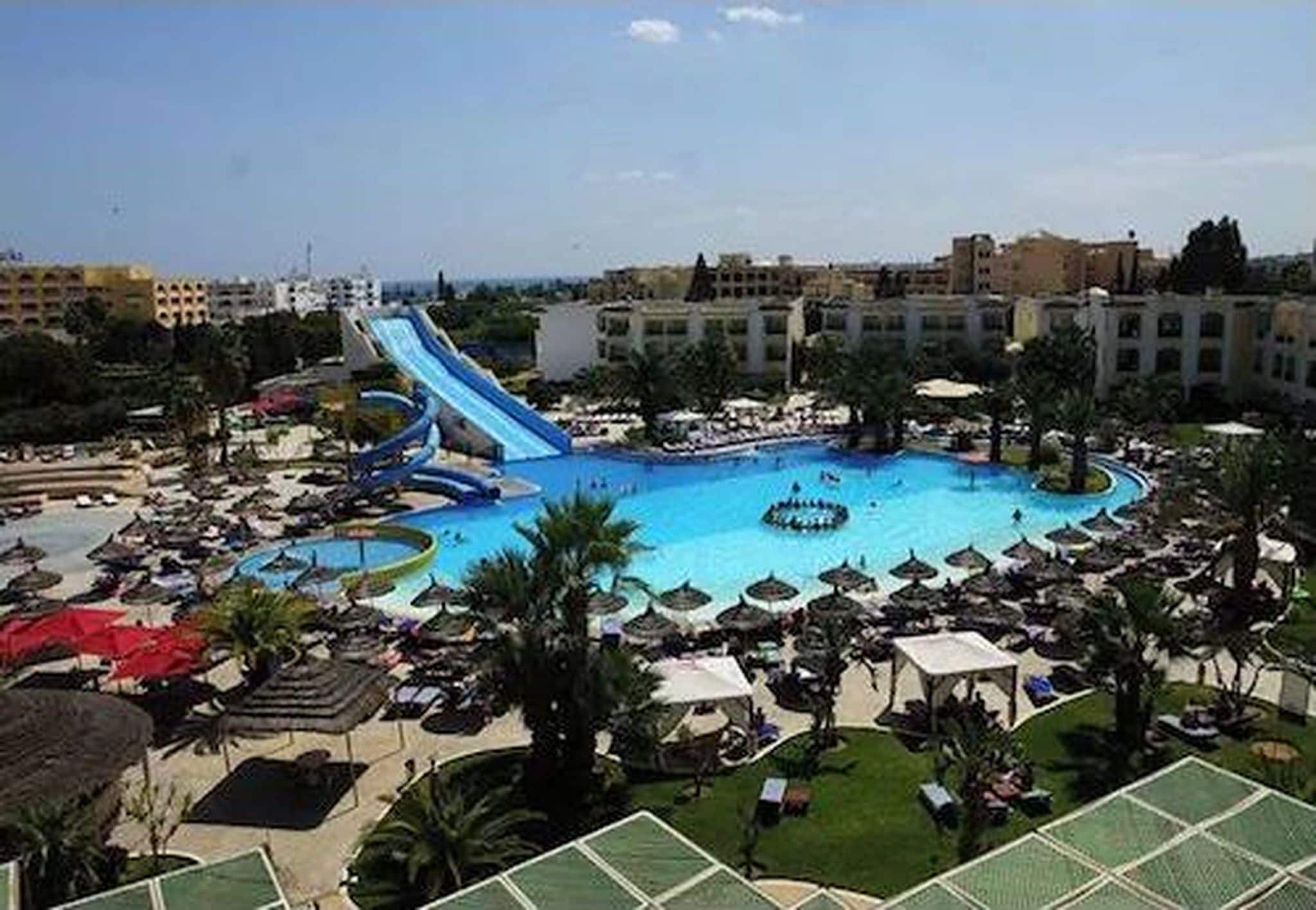 A resort with a large central pool, multiple water slides, and a surrounding lounge area with umbrellas.