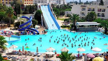 A large swimming pool with multiple slides and a busier area with umbrellas and lounge chairs.