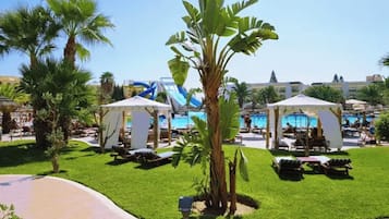 A resort pool area with palm trees, lounge chairs, and a water slide.