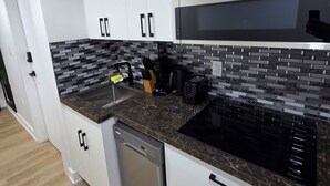 A modern kitchen with white cabinets, a black countertop, and a built-in microwave. - Stylish Studio Suite w/ Private Entrance | Parking (Brampton)
