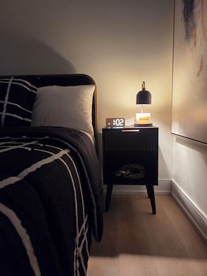 Une chambre à coucher avec un lit, une table de chevet avec une horloge et une œuvre d’art accrochée au mur.