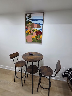 Un coin repas avec une table ronde en bois et quatre chaises, un tableau accroché au mur et une prise électrique sur le mur.