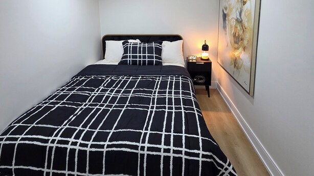 A bedroom with a bed, a nightstand, a wall-mounted artwork, and a ceiling vent. - Stylish Studio Suite w/ Private Entrance | Parking (Brampton)