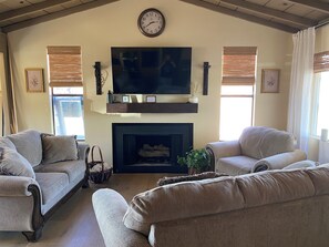 A living room with two sofas, a fireplace, a mounted television, and a clock on the wall. - 3BR Historic Retreat• Mountain Views •RV Parking (Unknown)