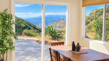 A dining area with a table and chairs, a view of a mountainous landscape through large glass doors, and a potted plant on the left.
