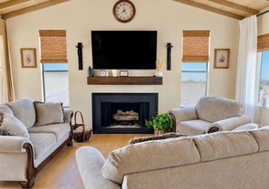 Una sala de estar con dos sofás, una chimenea, un televisor de pantalla plana y un reloj en la pared.