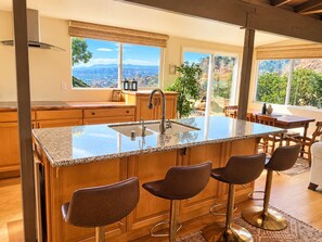 A kitchen with a large island, bar stools, and a view of mountains through large windows. - 3BR Historic Retreat• Mountain Views •RV Parking (Unknown)