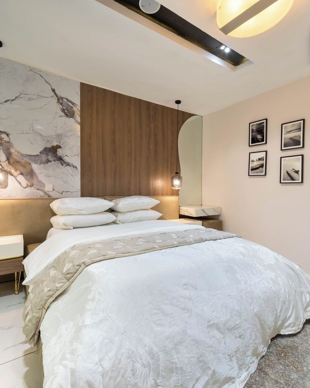 Ein modernes Schlafzimmer mit einem großen Bett, einem Holz-Kopfteil, einer Marmorwand und einem Spiegel.