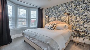 Ein Schlafzimmer mit einem Bett, einem Fenster mit Jalousien, einer Wand mit Blumenmuster und einer Stehlampe.