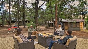Un grup de persones assegudes al voltant d'una xemeneia exterior, amb arbres i un edifici petit al fons.