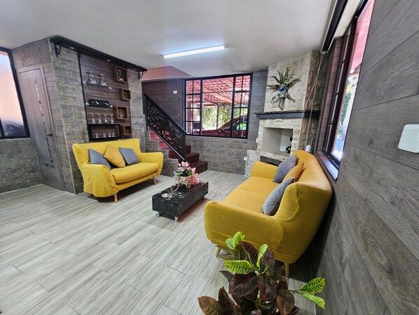 Un salón moderno con un sofá amarillo, una mesa de centro y una escalera que lleva a un área exterior.