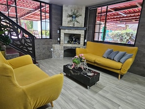 A living room with a yellow sofa, a black coffee table with decorative items, a fireplace, and a staircase with red railings.