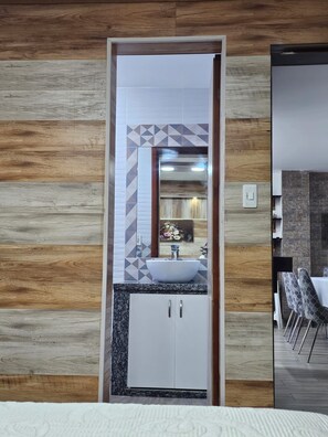 Un baño con pared de madera, un lavamanos blanco y un espejo.