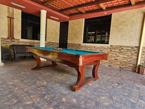 Una mesa de billar en un espacio techado con paredes de piedra y techo rojo.