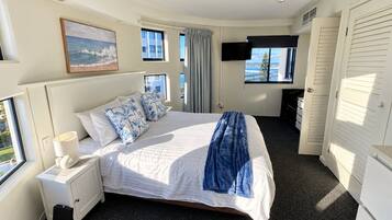 A hotel room with a bed, a bedside table with a lamp, a TV mounted on the wall, and a window with a view.