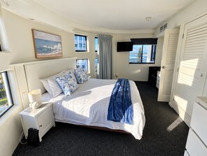 Quarto de hotel com cama, mesa de cabeceira com abajur, televisão na parede e janela com vista.