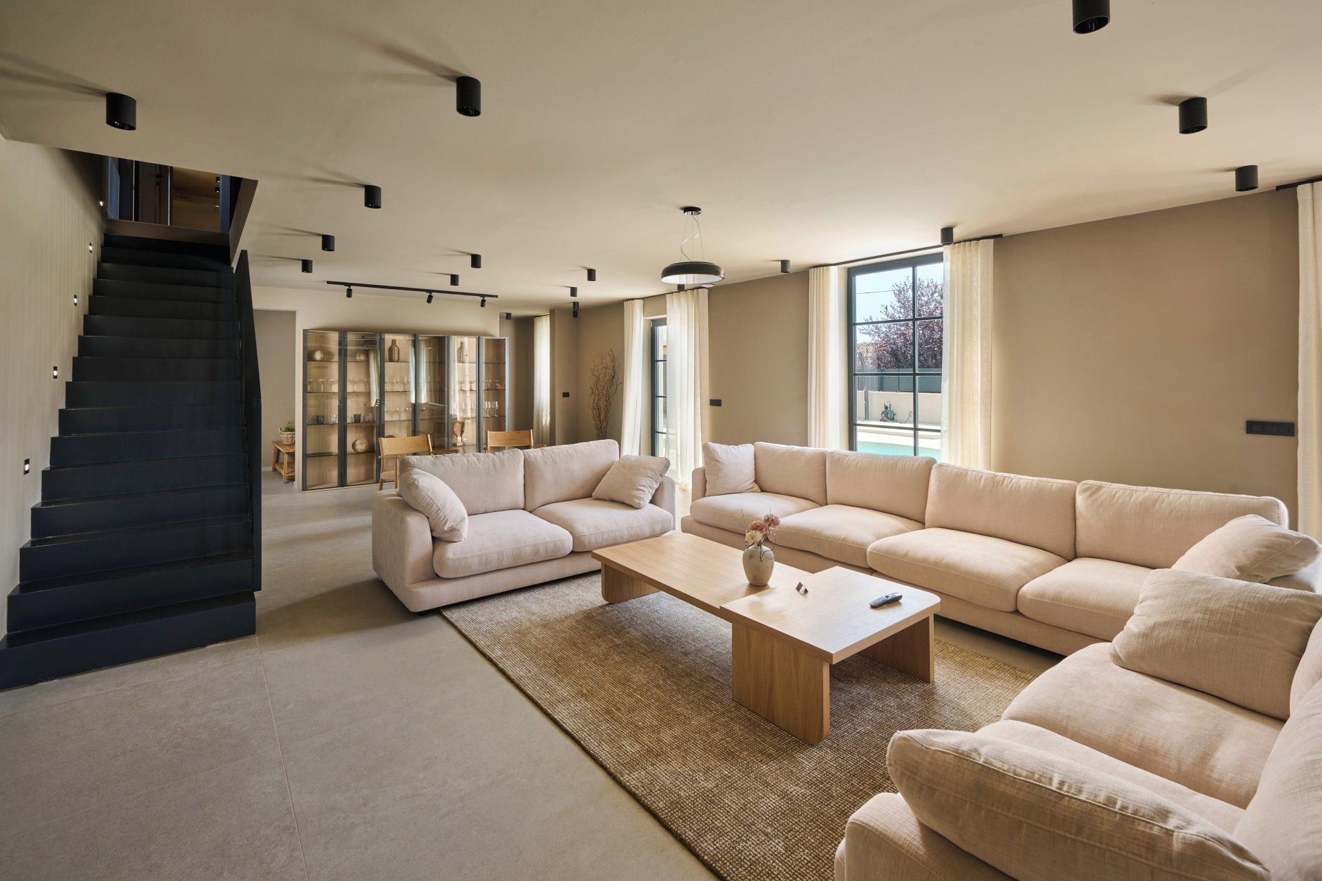 A modern living room with a staircase, a sectional sofa, a coffee table, and a glass cabinet.