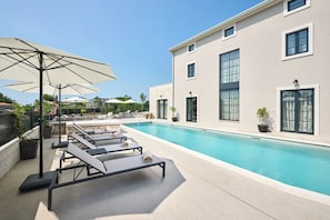 A modern pool area with lounge chairs and umbrellas, a clear sky, and a building with large windows. - Luxury Villa Madora for up to 12 guests by Istrabook (Poreč)