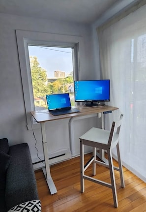 Ein Zimmer mit Schreibtisch, zwei Laptops, einem Stuhl und einem Fenster.
