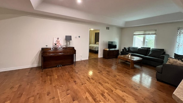 Een ruime woonkamer met houten vloeren, een donkerbruine bank en salontafel, en een televisie op een dressoir.