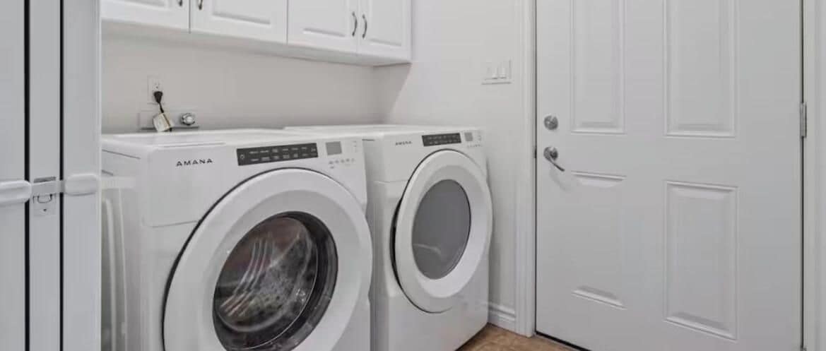Une buanderie équipée de deux machines à laver à chargement frontal blanches, avec un meuble blanc placé au-dessus.