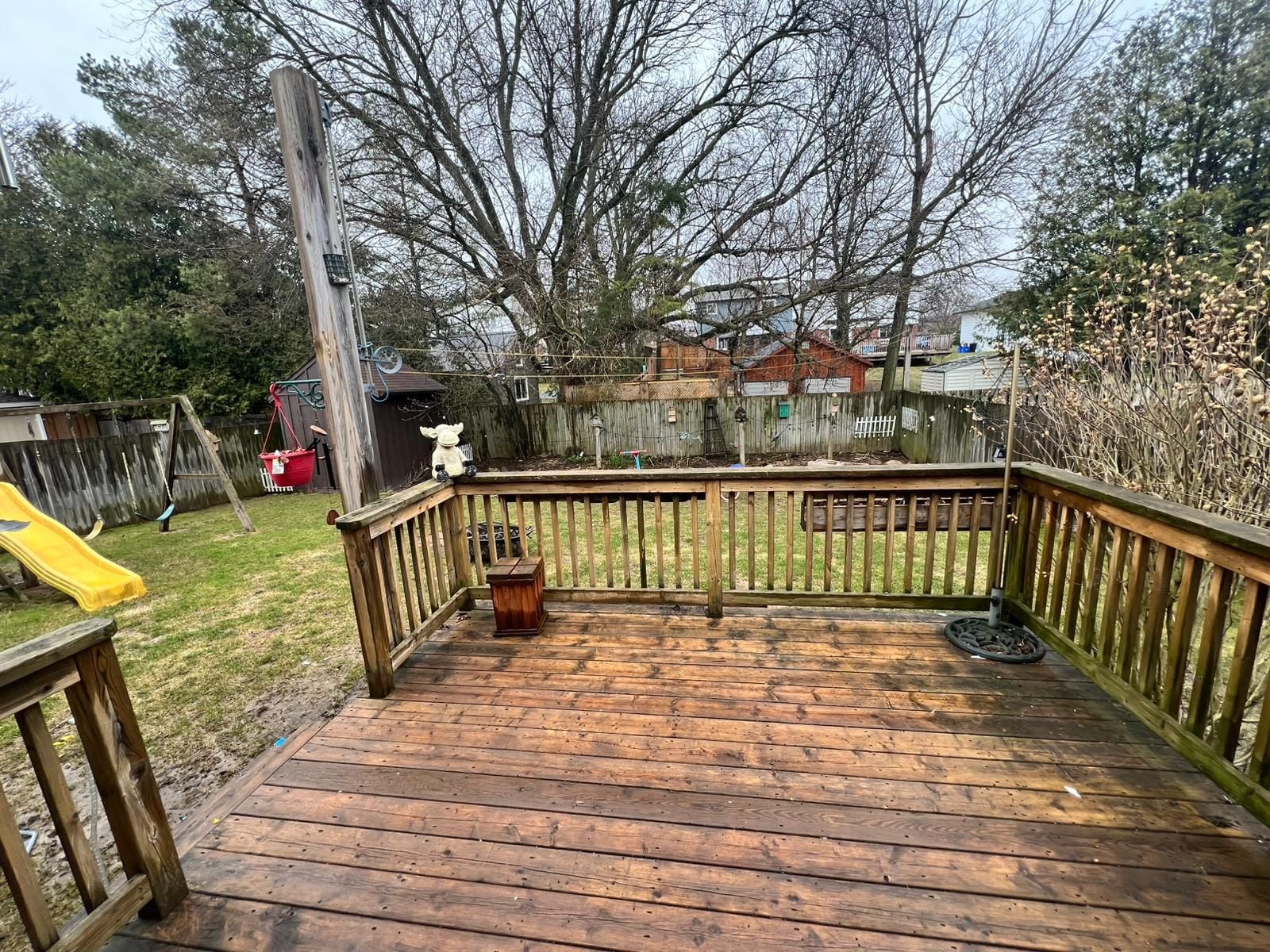 A wooden deck with a railing, a swing set, and a slide in the background.