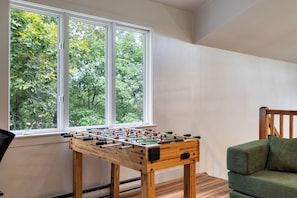 Ein Zimmer mit einem Holztischfußball und einem Fenster mit Blick auf Bäume.