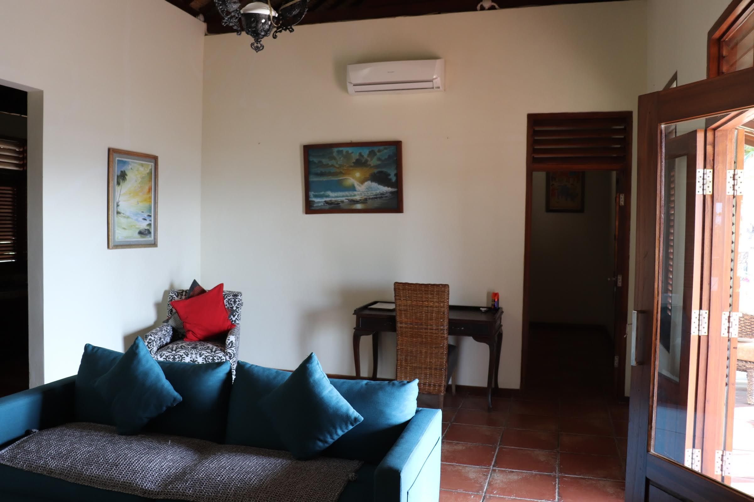 A living room with a sofa, a painting, an air conditioning unit, and a dining area.