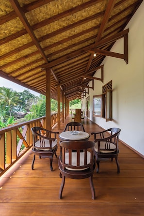 A covered outdoor seating area with wooden furniture and a view of the surrounding greenery.