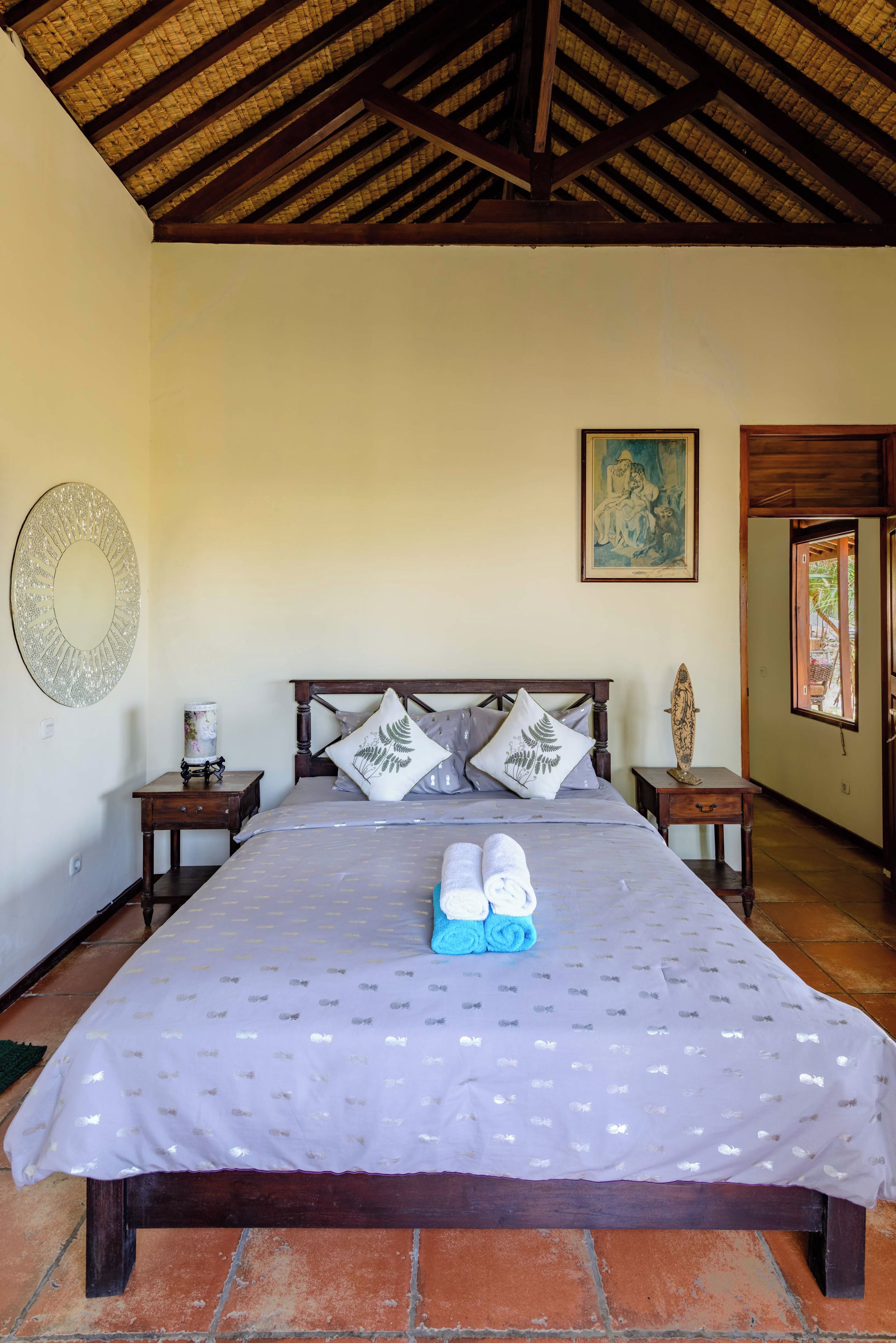 A bedroom with a large bed, two nightstands, a wall-mounted mirror, and a painting.