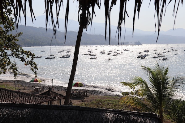 A beach with boats, umbrellas, and a thatched-roof structure.