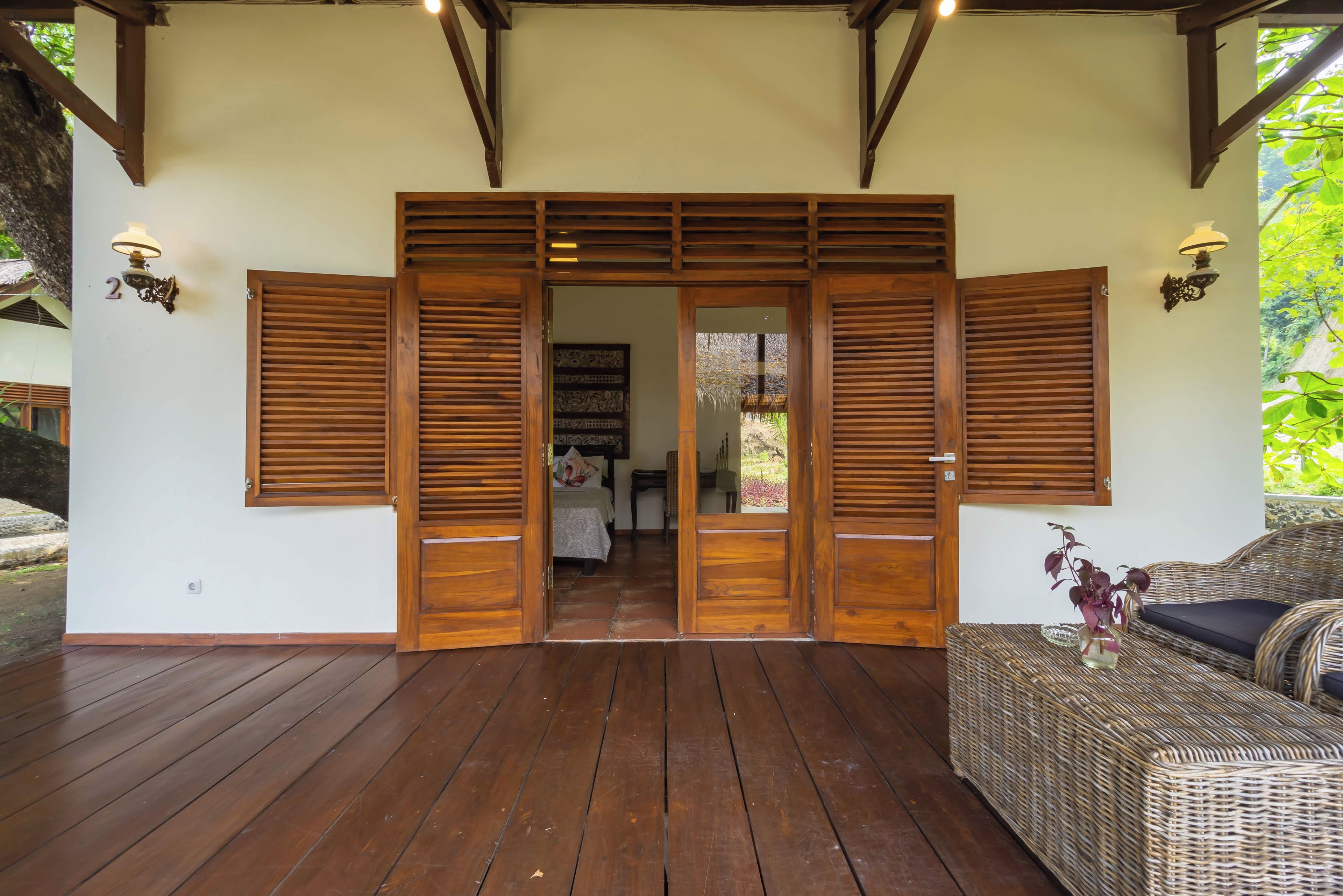 A wooden door with a sliding mechanism, a wicker sofa, and a small table with a vase.