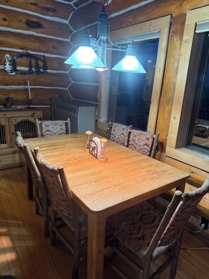 Een houten eettafel met stoelen, een gedessineerd tafelkleed en een hanglamp.